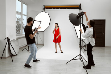 Professional photographer and assistant working with beautiful model in modern photo studio