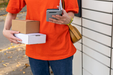 A woman with a phone near the self-service mail terminal. Parcel delivery machine. Person holding a...
