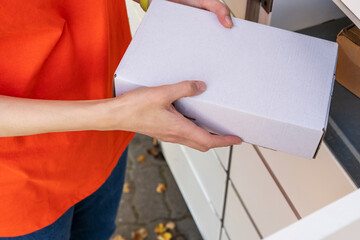Person holding a cardboard box. A woman with a box in her hands near the self-service mail terminal. Parcel delivery machine. Mail delivery and post service, online shopping, e commerce concept 