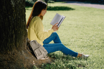 Young woman reading book near tree in park on sunny day