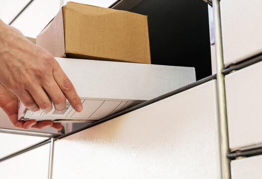 Person holding a cardboard box. A woman with a box in her hands near the self-service mail terminal. Parcel delivery machine. Mail delivery and post service, online shopping, e commerce concept	