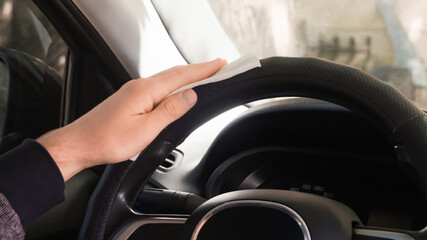 Man cleaning steering wheel with wet wipe in car, closeup. Protective measures