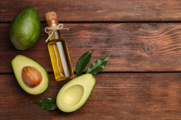 Glass bottle of cooking oil and fresh avocados on wooden table, flat lay. Space for text