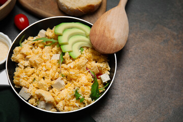 Frying pan with delicious scrambled eggs, tofu and avocado on textured table. Space for text