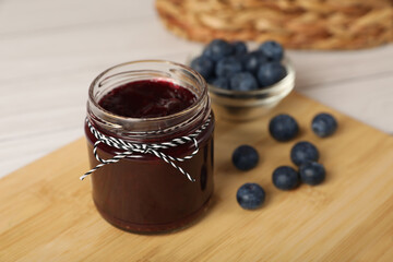 Jar with tasty blueberry jam and berries on wooden table. Space for text