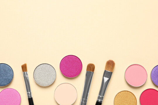 Different beautiful eye shadows and makeup brushes on beige background, flat lay. Space for text