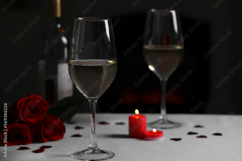 Poster Glasses of white wine, rose flowers and burning candles on grey table against blurred background. Romantic atmosphere