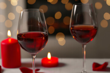 Glasses of red wine and burning candles against blurred background, space for text. Romantic atmosphere