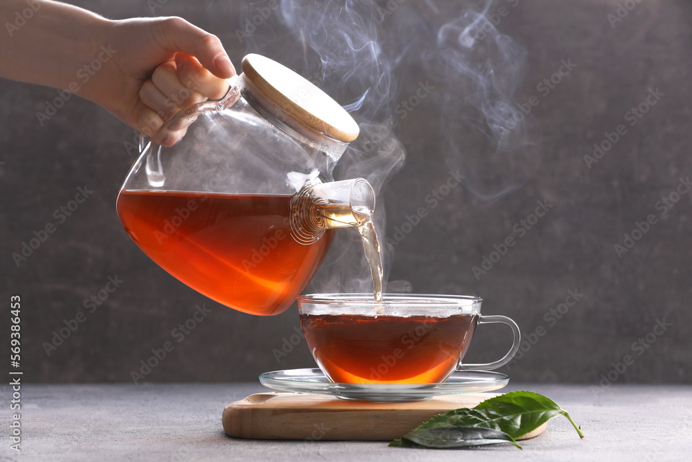 Wall mural woman pouring aromatic hot tea into glass cup on light grey table, closeup