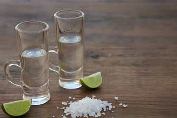 Mexican tequila shots with lime slices and salt on wooden table, closeup. Space for text