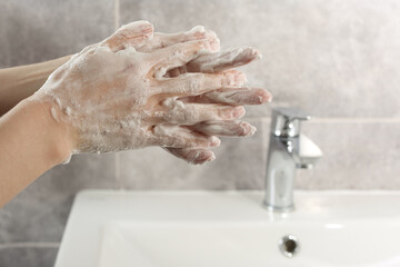 Woman washing hands with cleansing foam near sink in bathroom, closeup