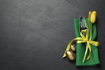 Cutlery set, painted eggs and beautiful flower on black table, flat lay with space for text. Easter celebration