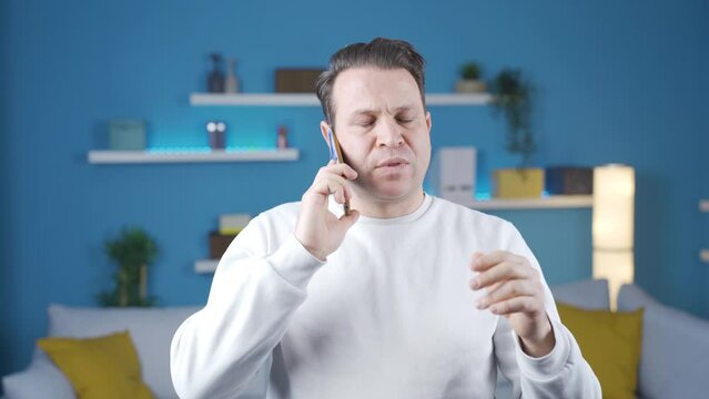 The man talking on the phone at home is trying to explain himself, he speaks calmly and without panic.
The man talking on the phone at home is telling something in a calm and relaxed manner.
