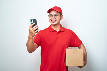 Asian courier man in red uniform smiling look at his smartphone while holding cardboard box parcel