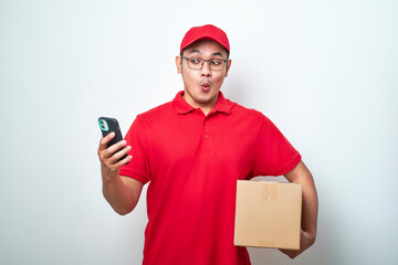 Asian courier man in red uniform smiling look at his smartphone while holding cardboard box parcel