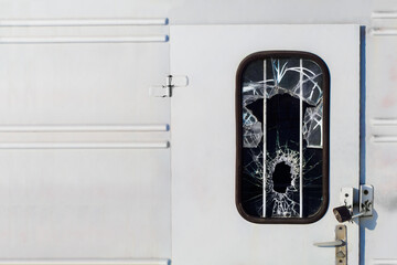 A broken glass window and bars in a metal door. Sharp shards and glass texture. The door to the...