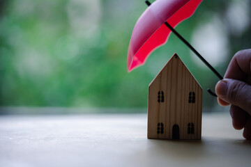House insurance concept. Toy house defended by red umbrella on blur nature background with copy space