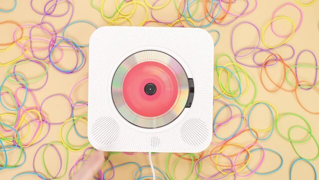 Hands put vintage white stylish portable CD player on bright yellow background full of rubber bands. Using vintage cd player for music listening pink compact disc