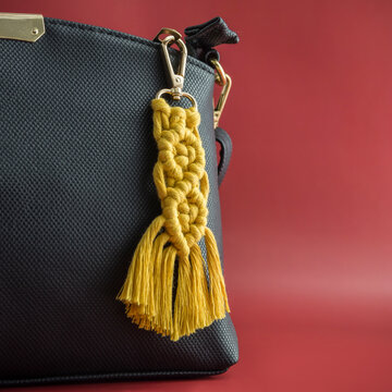 Close-up view of the handmade Macrame key chain hanging on the black hand bag isolated on the red background.