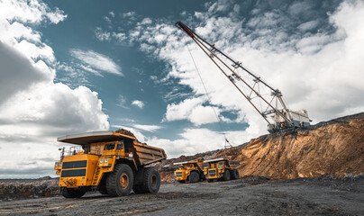 Large quarry dump truck. Big yellow mining truck at work site. Loading coal into body truck. Production useful minerals. Mining truck mining machinery to transport coal from open-pit production - obrazy, fototapety, plakaty