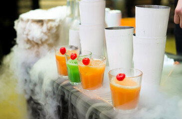 Colorful smoothies in glass cups for sale at a bar counter. In a cloud of nitrogen.