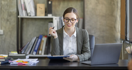 Portrait of smiling pretty young business woman in wearing glasses sitting on her workplace office, business finance concept.