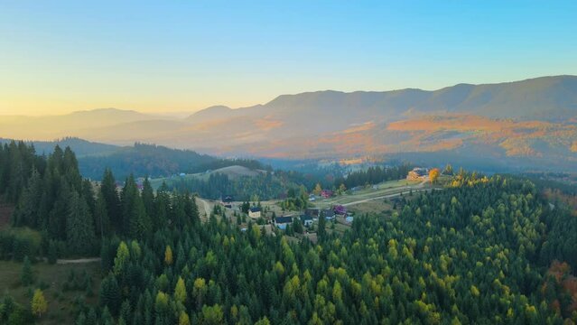 Wooded hills of Carpathian mountains in Ukraine with small traditional village houses at sunset. Brightly illuminated with setting sun evergreen woods with scattered local homes at fall season