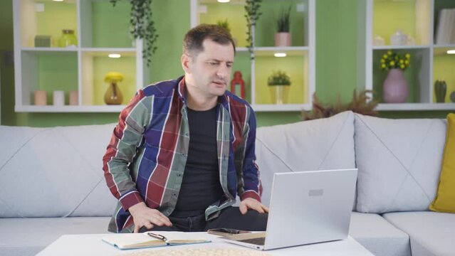 Man with backache from sitting in wrong position while working.
His back and neck are starting to hurt because of the man who works from home sitting in the wrong position.
