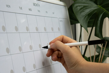 Female hand writing with marker on Monthly PLANNER. Magnetic board with the days of the month. Place to enter important matters schedule. Whiteboard Planner magnetic monthly template