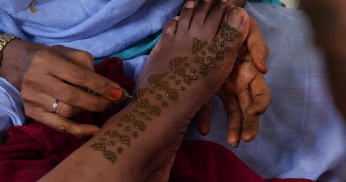 A shot of female hands painting a black foot with henna