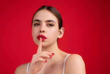 Girl showing shhh sign with finger near lips, standing over studio background. Women emotions. Secret young woman saying hush be quiet, shhh gesture. Quiet and silence. Human face expressions.