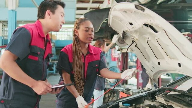 Male professional automotive supervisor advises and inspects Black female mechanic worker about liquid engine oil at car garage, service maintenance, and fixing specialist occupations auto industry.