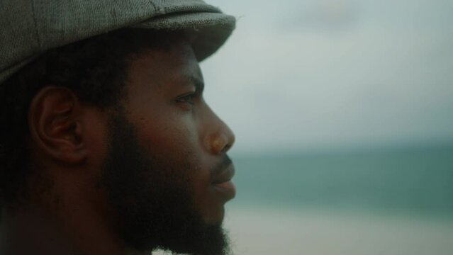 Close-up of handsome, bearded young black man looks introspectively out to sea. High quality 4k footage