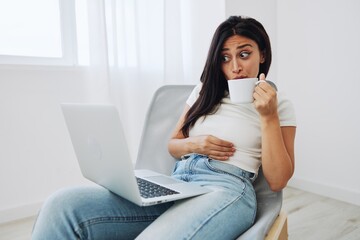 Woman relaxing at home sitting in a chair and watching a movie on her laptop with a cup of tea, the surprise of watching, freelancer lifestyle