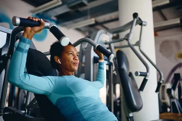 Foto auf Acrylglas Fitness African American athletic woman using exercise machine during sports training in health club.