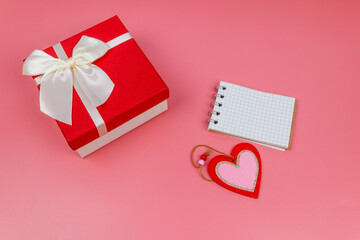 Red gift box, Valentine heart and blank notepad on pastel pink background. Top view, flat lay. Valentine Day concept