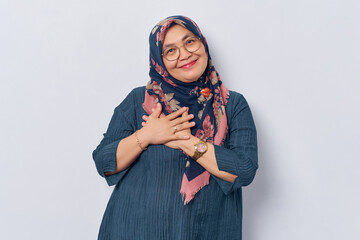 Elderly smiling Asian Muslim woman 50s wearing hijab in glasses holding palms on chest over heart...