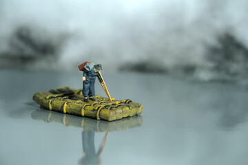 Miniature people toy figure photography. An old man refugees with crutch riding the raft alone,...