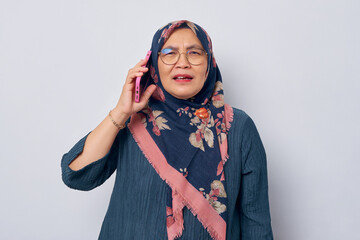 Shocked Asian Muslim woman 50s wearing hijab in glasses talking on mobile phone, looking at camera with happy facial expression isolated on white background. People islam religious concept