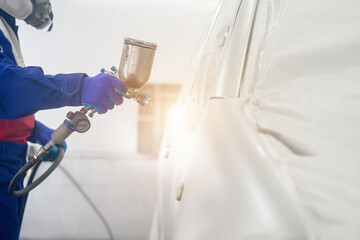 A mechanic worker is using a blue spray gun to paint a car. Car painter in car paint room