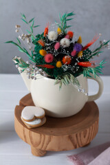 A small teapot is filled with a bouquet of dried flowers