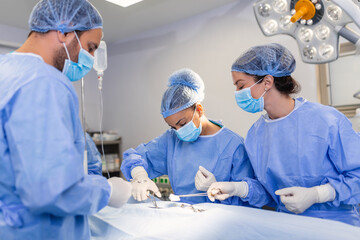 Surgeons operating below lighting equipment. Male and female doctors are wearing blue scrubs. They are working in hospital.