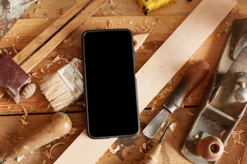 Top view shot of cell phone with empty display on table among the shavings and set of carpentry tools, copy space for advertisement or promotional text.