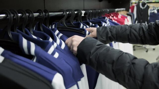 Woman in clothing store buys jacket choosing size on showcase hanger.