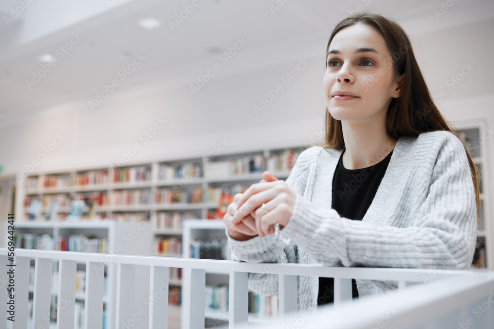 Wall mural University, thinking and woman in library for knowledge, learning and academic research in building. Education, college and young female student with ideas, vision and happy mindset for future goals