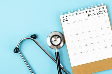 A April 2023 deskcalendar and medical stethoscope medical on blue background, schedule to check up healthy concepts.
