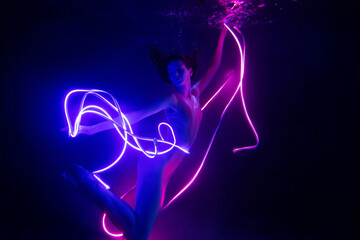 Gymnast shows underwater performance in neon light. Soft blurred focus