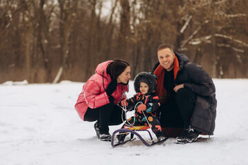 parenthood, season and people concept - happy family with child on sled walking in winter outdoors