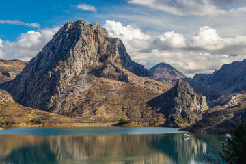 Panoramic view of a mountain lake with clear turquoise-green water against the background of a road and a village of farmers