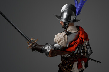 Portrait of conquistador dressed in plate armor posing with sword looking away.